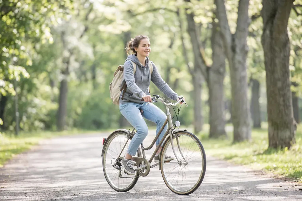 Teenage girl smiling as she rides a bicycle along a tree-lined park path
